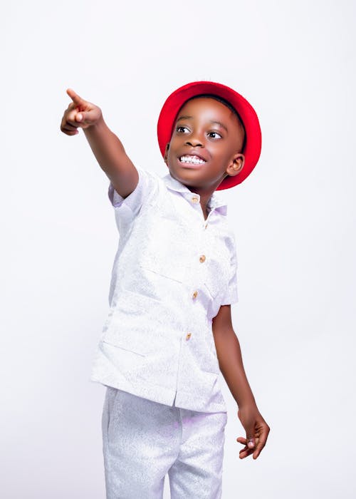A young boy in a white shirt and red hat pointing