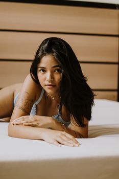 Young woman with tattoos lying on bed in lingerie, captured in soft light.
