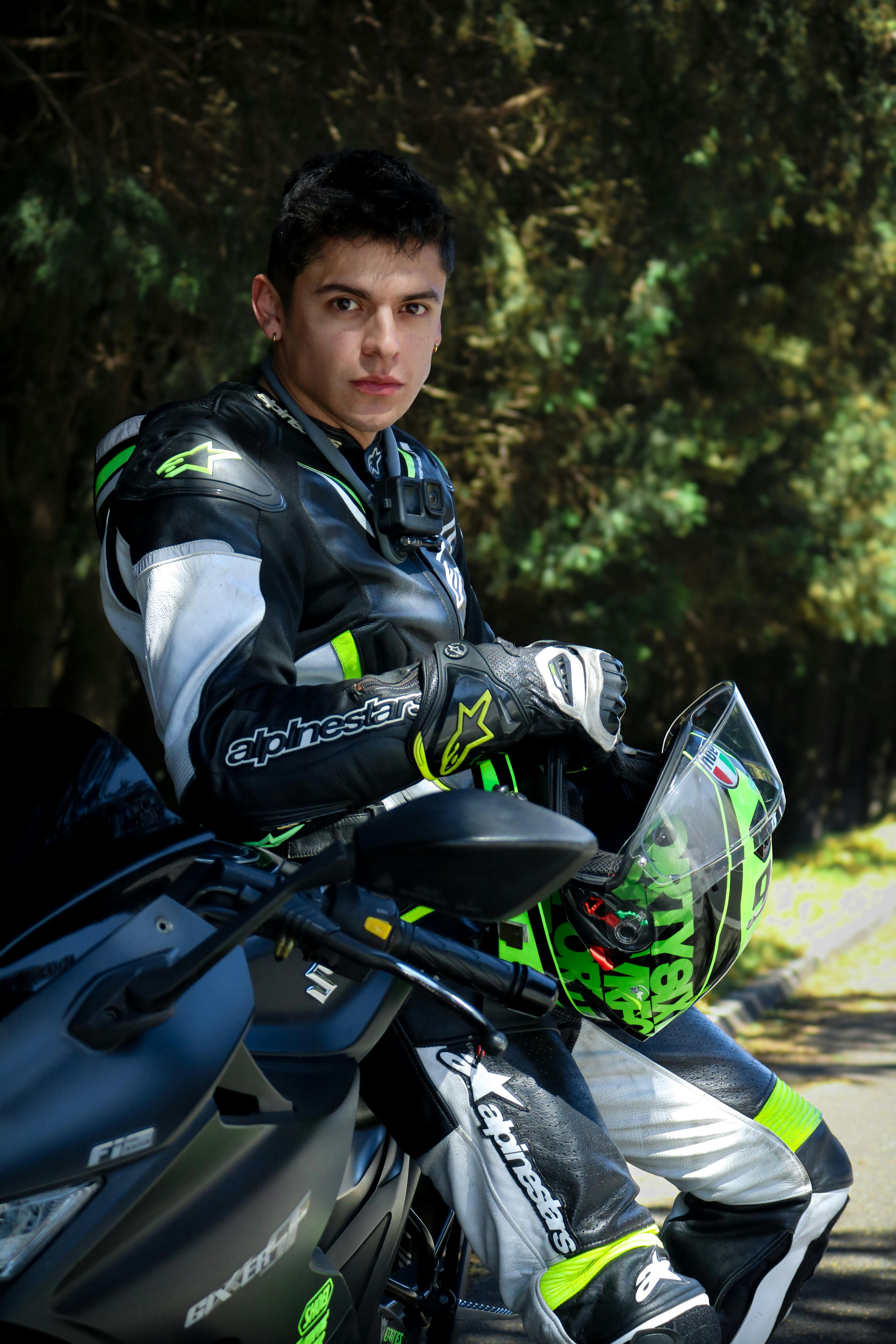 Young man in leather racing suit with helmet, sitting on a sport motorcycle outdoors.