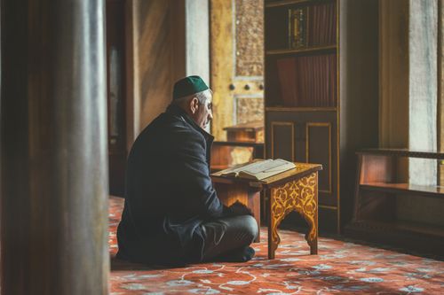 Free Elderly man reading Koran, seated in a historic Istanbul mosque, reflecting spirituality and contemplation. Stock Photo