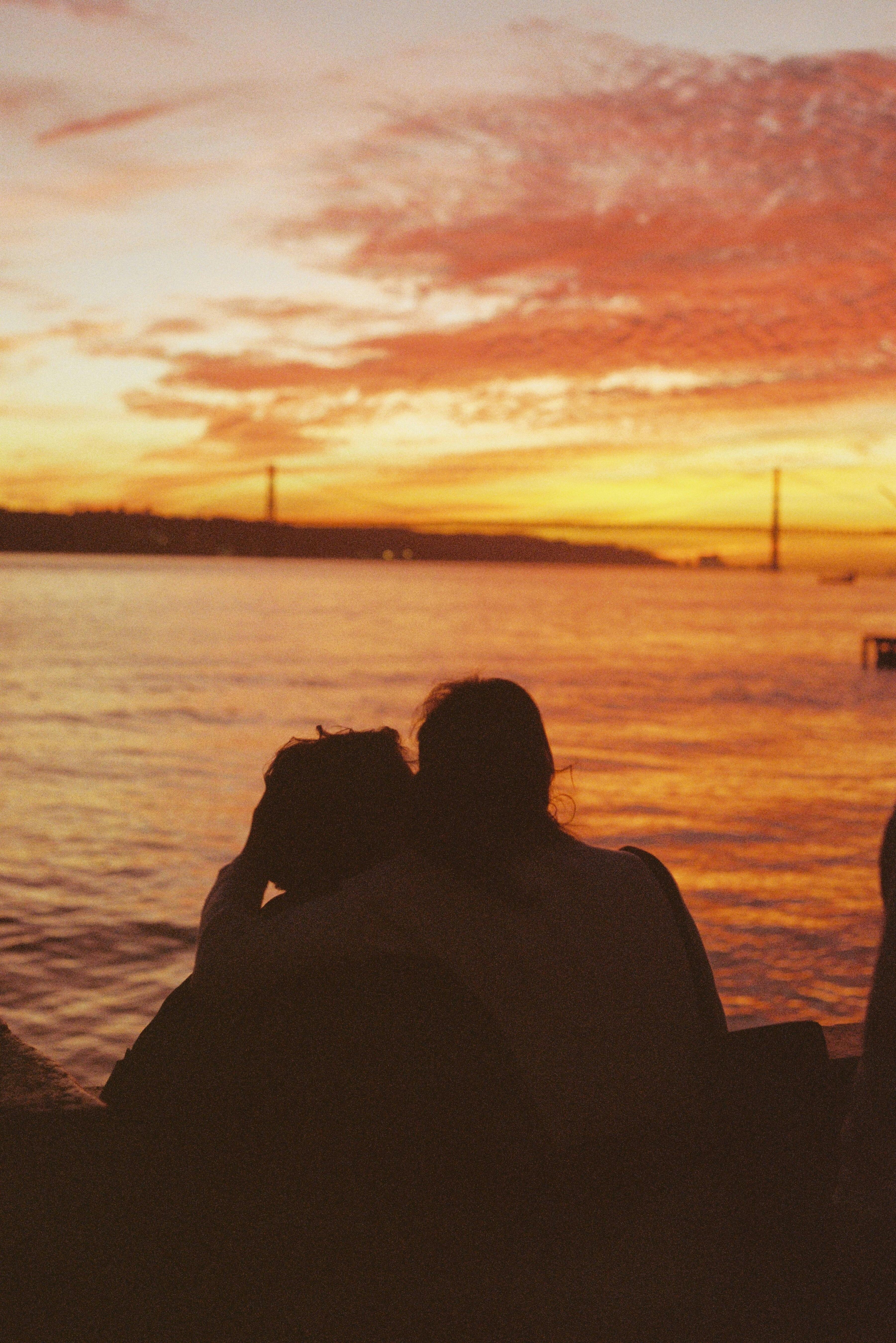 Silhouette of a couple embracing at sunset overlooking Lisbon's scenic bridge and ocean.