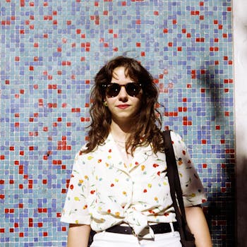Stylish woman in sunglasses and floral blouse posing against a colorful mosaic wall in Lisbon.