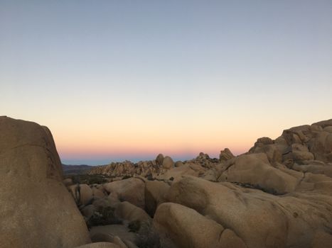 A tranquil view of rocky desert formations under a soft pastel sunset sky.
