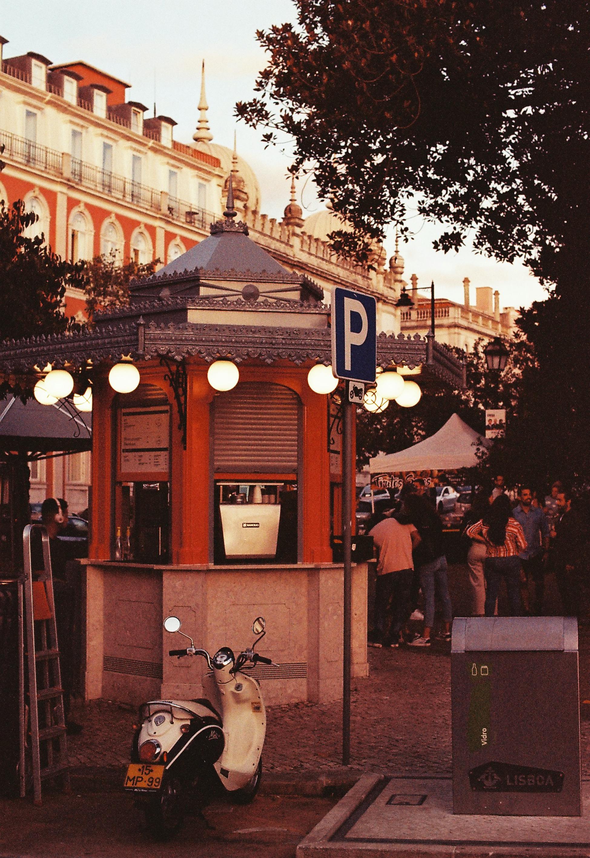 View of a cozy street booth and a scooter in Lisbon's urban landscape during sunset.