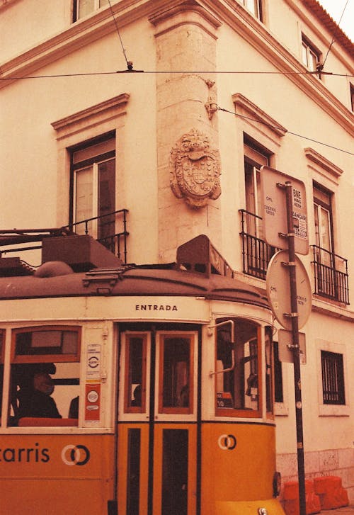 A yellow tram is parked in front of a building