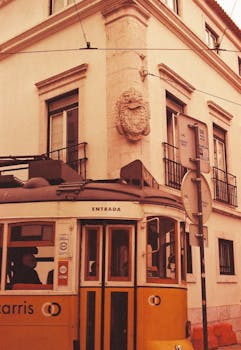 Vintage yellow tram passing through a historic street corner in Lisbon, Portugal.