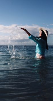 Woman in a hat playing with water at the beach, enjoying a sunny summer day.