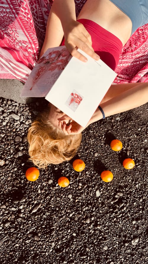 A woman laying on the ground with oranges and a book