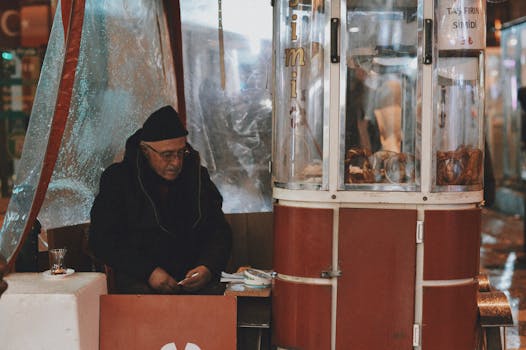 Elderly vendor sitting at a street food stall selling simit on a rainy day.