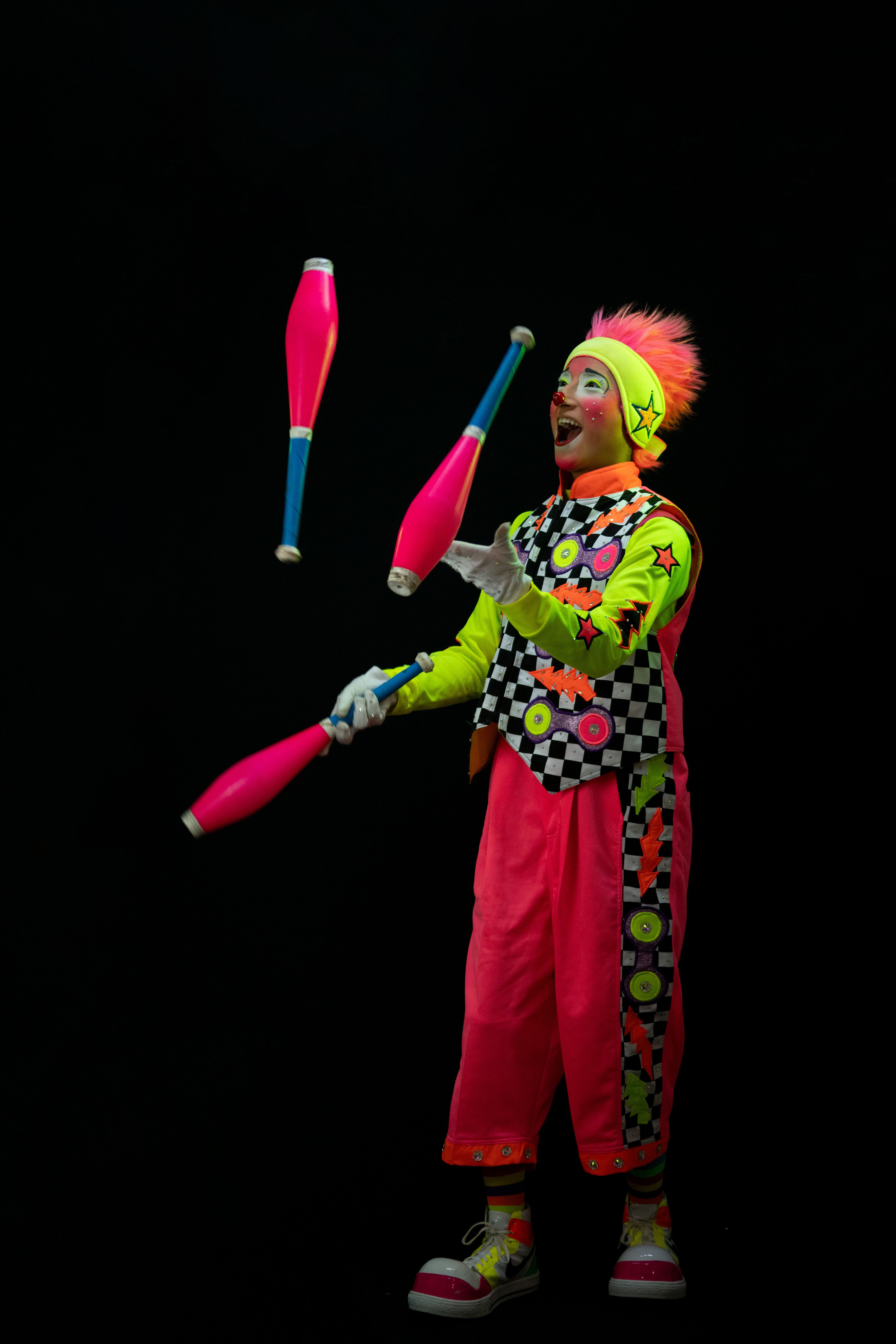 Colorful clown juggling clubs against a black background in a studio setting.
