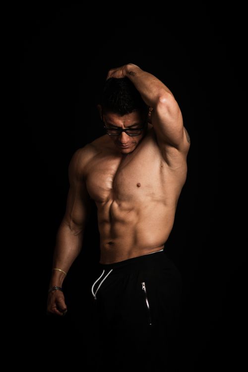 Free Portrait of a muscular man in glasses posing against a dark backdrop. Stock Photo