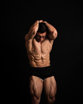 Portrait of muscular bodybuilder standing against a black background.