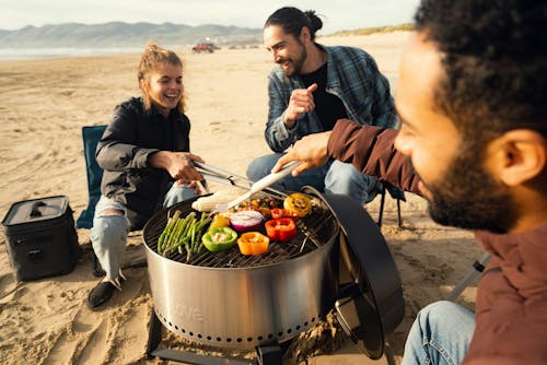 A group of people sitting around a grill on the beach