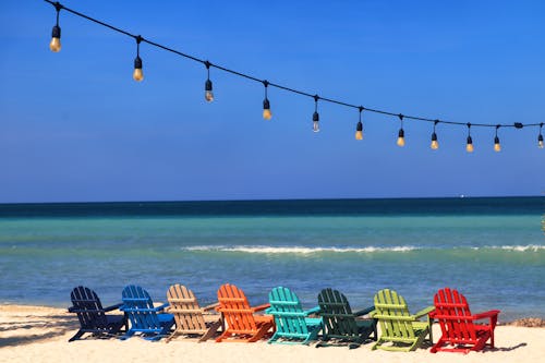 A row of colorful chairs on the beach with string lights
