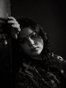 A dramatic black and white portrait of a teenage girl with a contemplative expression, shot indoors.