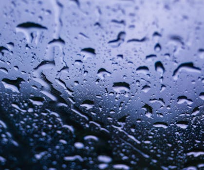 Close-up of raindrops on a window with a reflective blue sky background.