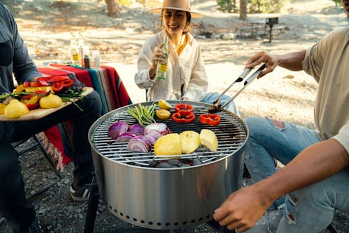 A group of people sitting around a grill with vegetables