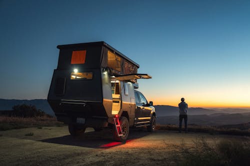 A man standing in front of a camper at dusk