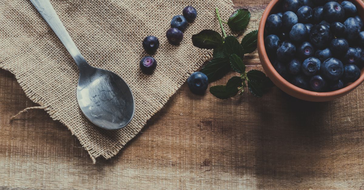 a bowl of fresh blueberries with a spoon, on a wooden table with natural light
