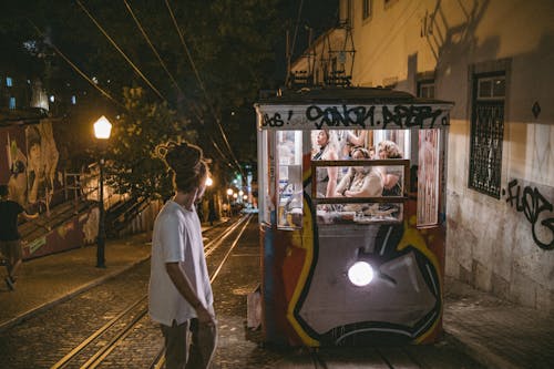 Man with Dreadlocks Walking near Vintage Tram with People on Street in Lisbon at Night