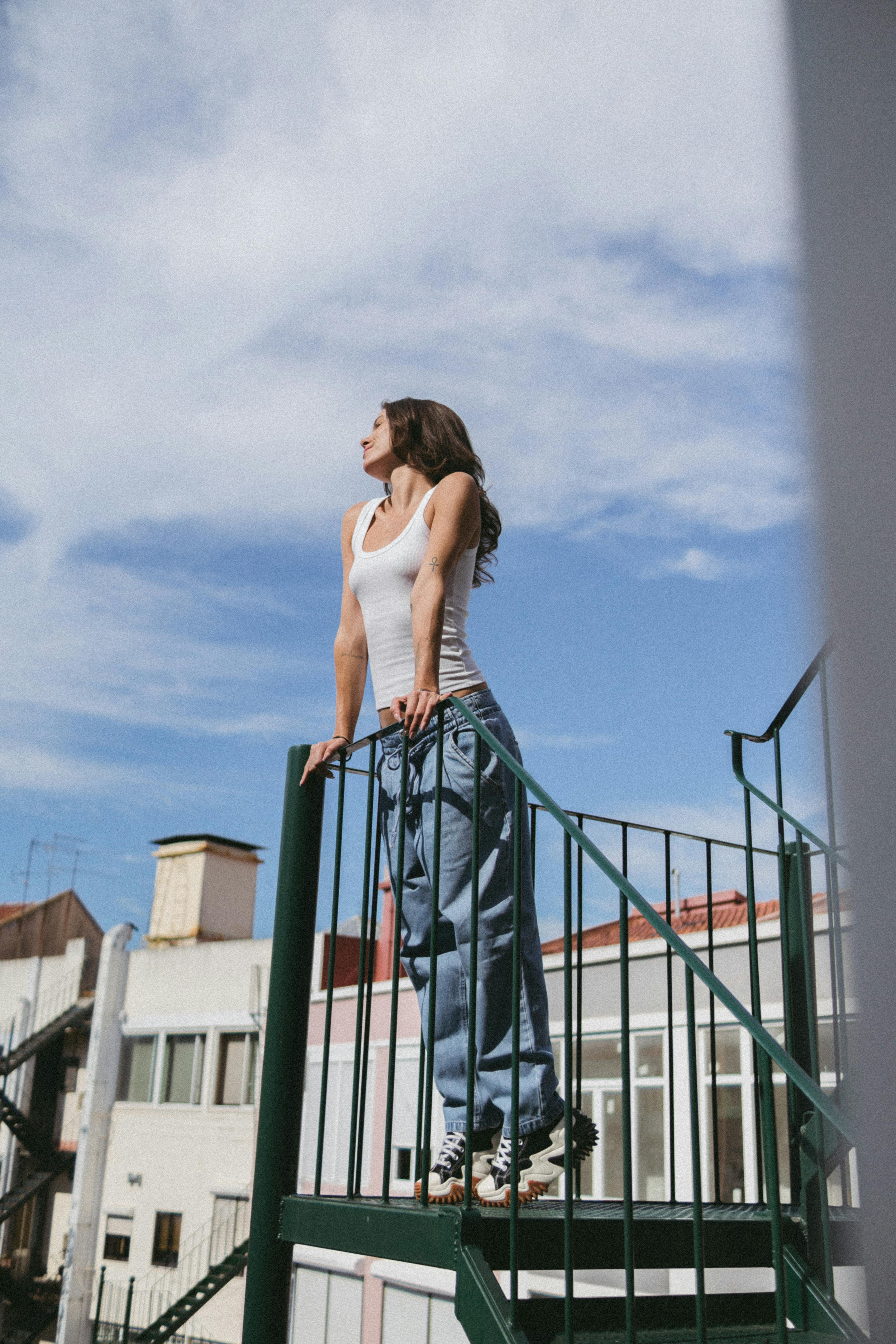 Stylish woman in jeans and tank top standing on a spiral staircase in Lisbon, Portugal, with an urban backdrop.