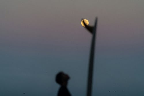 A man is silhouetted against the moon as he walks on the beach