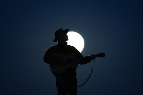 A silhouette of a man playing guitar in front of the moon
