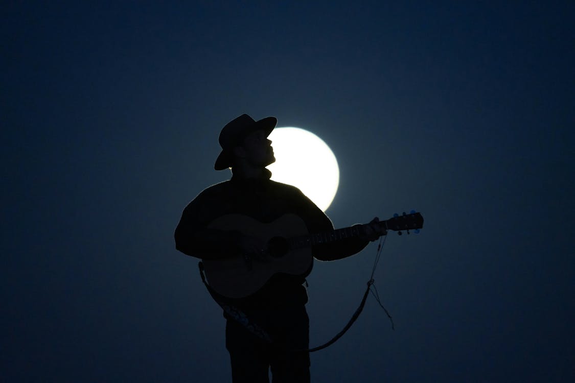A silhouette of a man playing guitar in front of the moon
