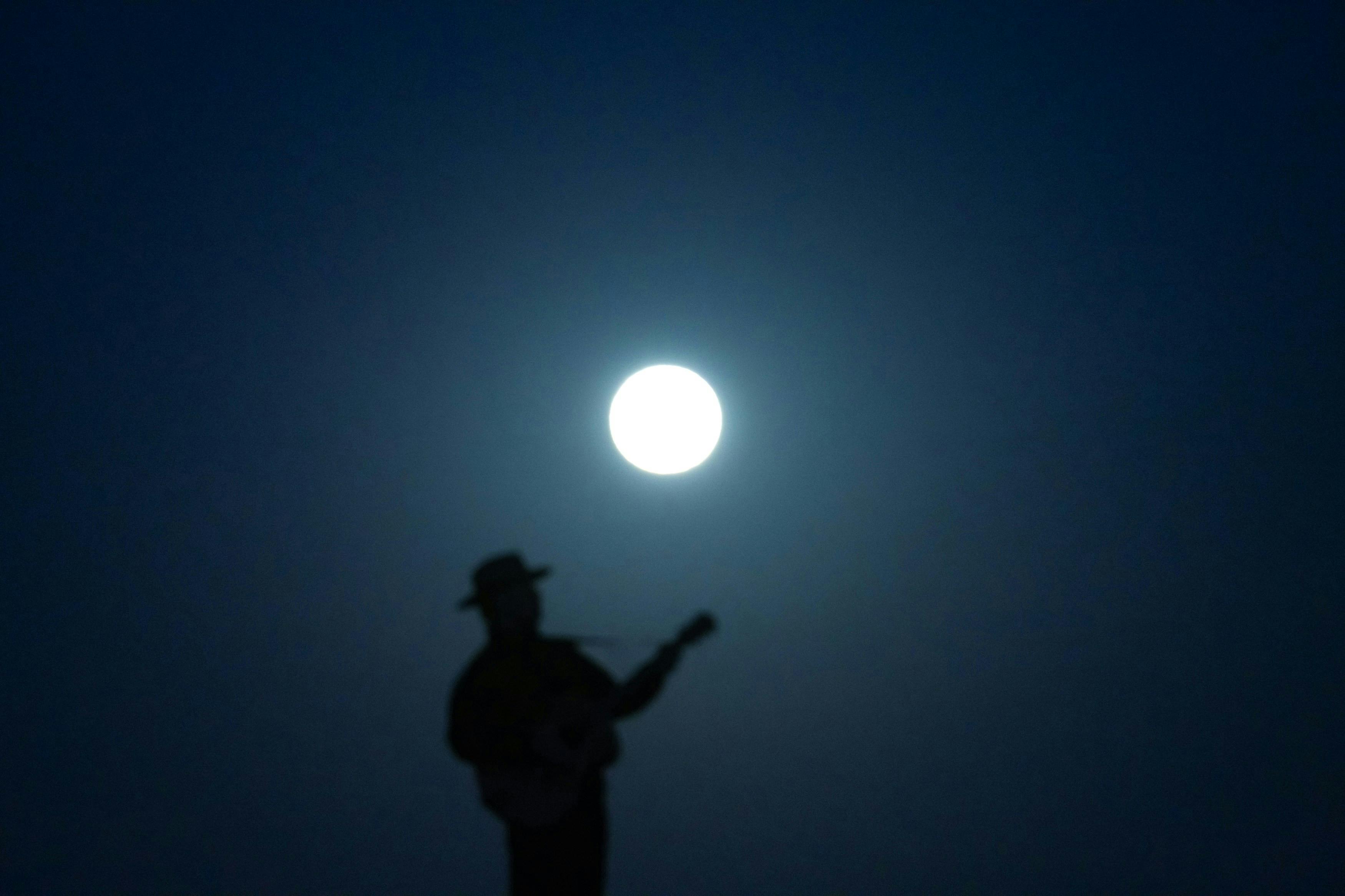 man plays guitar under full moon