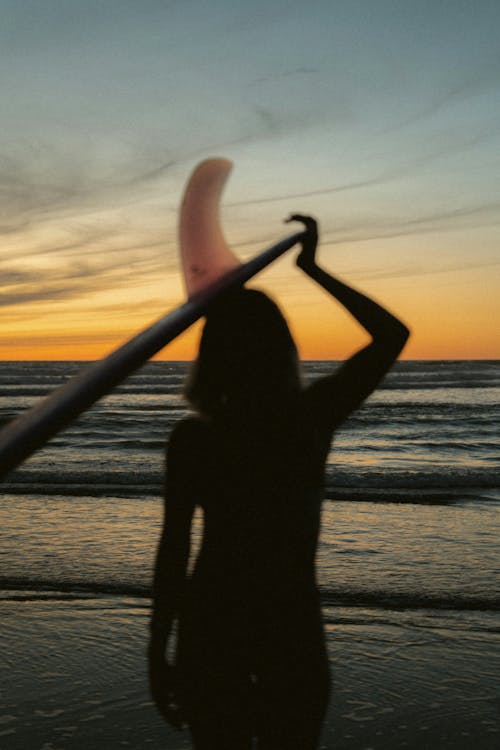 A woman holding a surfboard at sunset