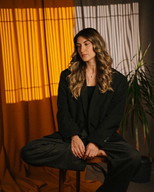 Free Stylish woman in a dark suit sitting on a chair with dramatic lighting indoors. Stock Photo