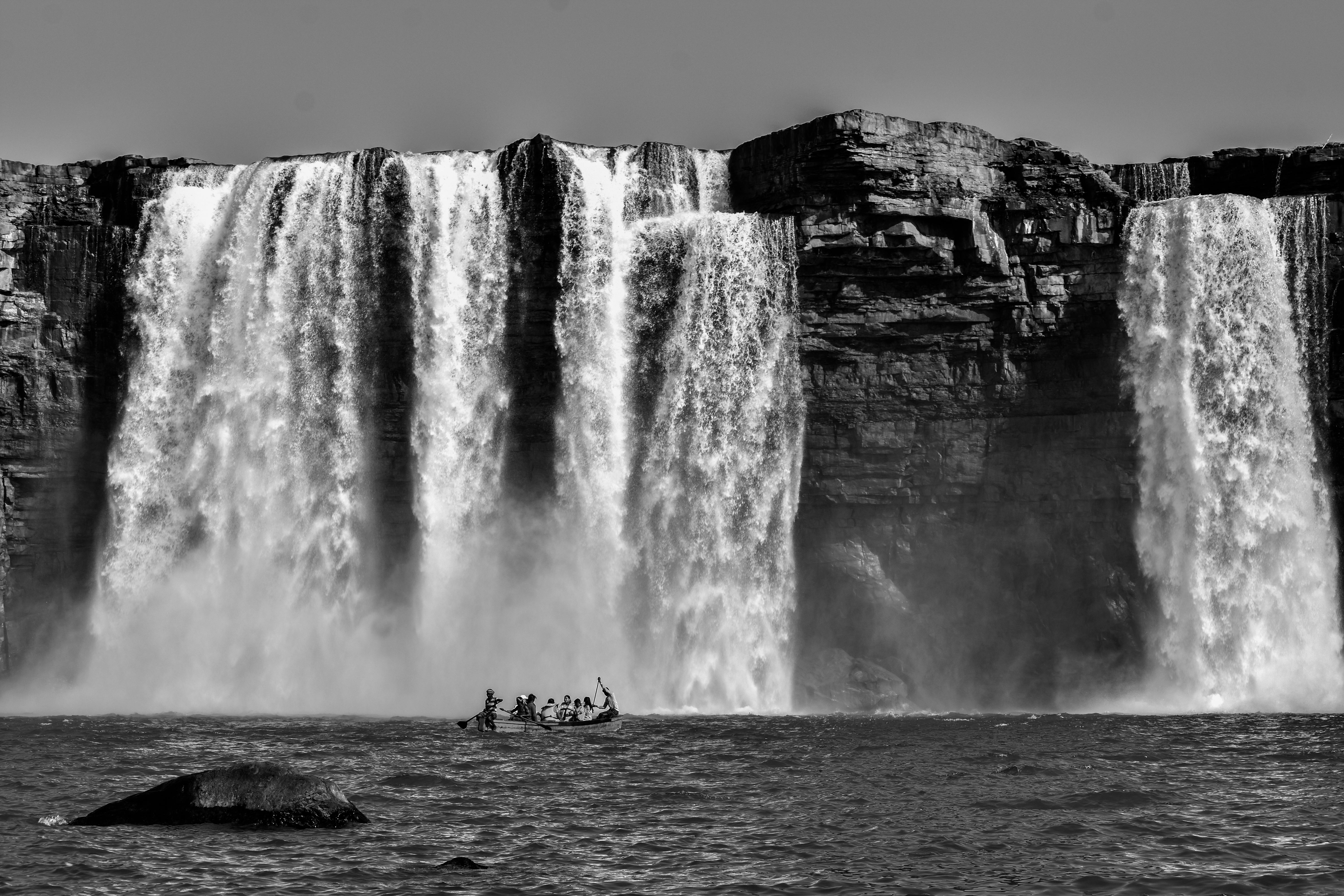 grayscale photography of people riding a boat near waterfalls