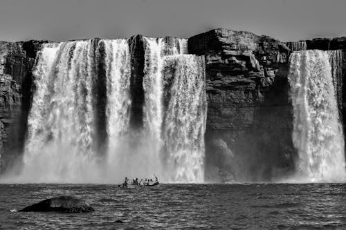 Grayscale Photography Of People Riding A Boat Near Waterfalls