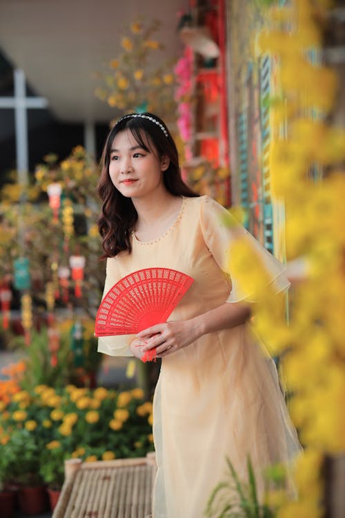 A woman in a yellow dress holding a red fan