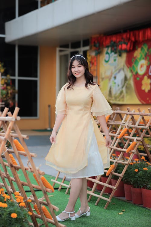 A woman in a yellow dress standing in front of a flower garden