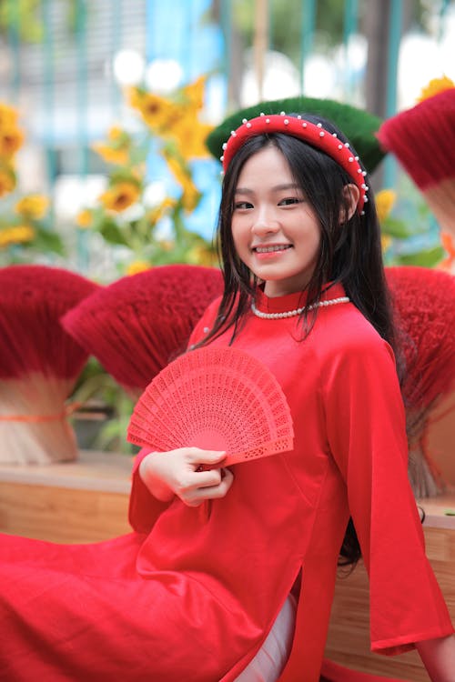 A woman in red holding a fan and smiling