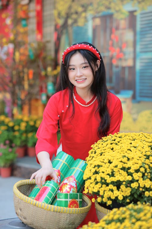 Young Model in Red Ao Dai Dress Next to Baskets of Flowers and Rice Cakes