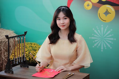 A woman in a yellow dress sitting at a table with a red paper