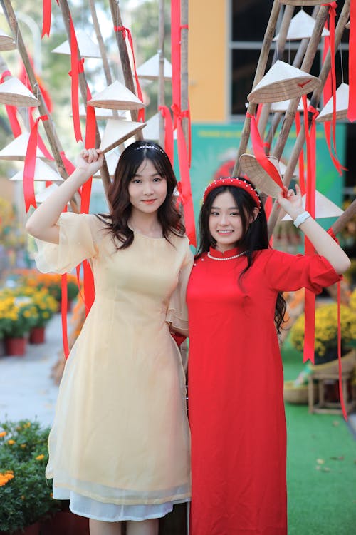Two asian women in red and yellow dresses pose for a photo