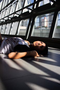 一名妇女躺在城市的地板上，周围阳光明媚，建筑现代