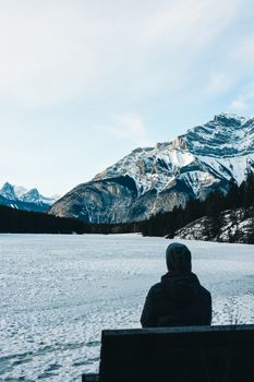 A person sits on a bench overlooking the snowy landscape and mountains in Banff, Canada.