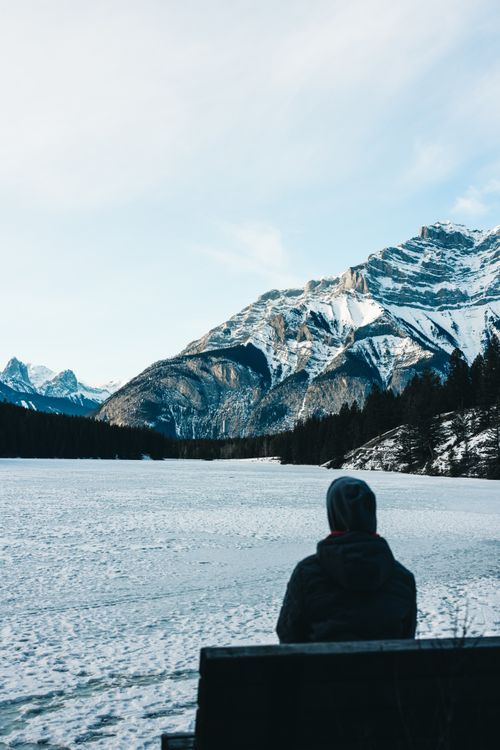 Free A person sits on a bench overlooking the snowy landscape and mountains in Banff, Canada. Stock Photo