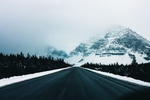 Free Snow-covered road leading towards misty mountains in Jasper National Park, Alberta, Canada. Stock Photo