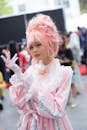 节日户外，一名身着优雅粉色角色扮演服装的年轻女子摆出姿势，展示着服装的复杂细节