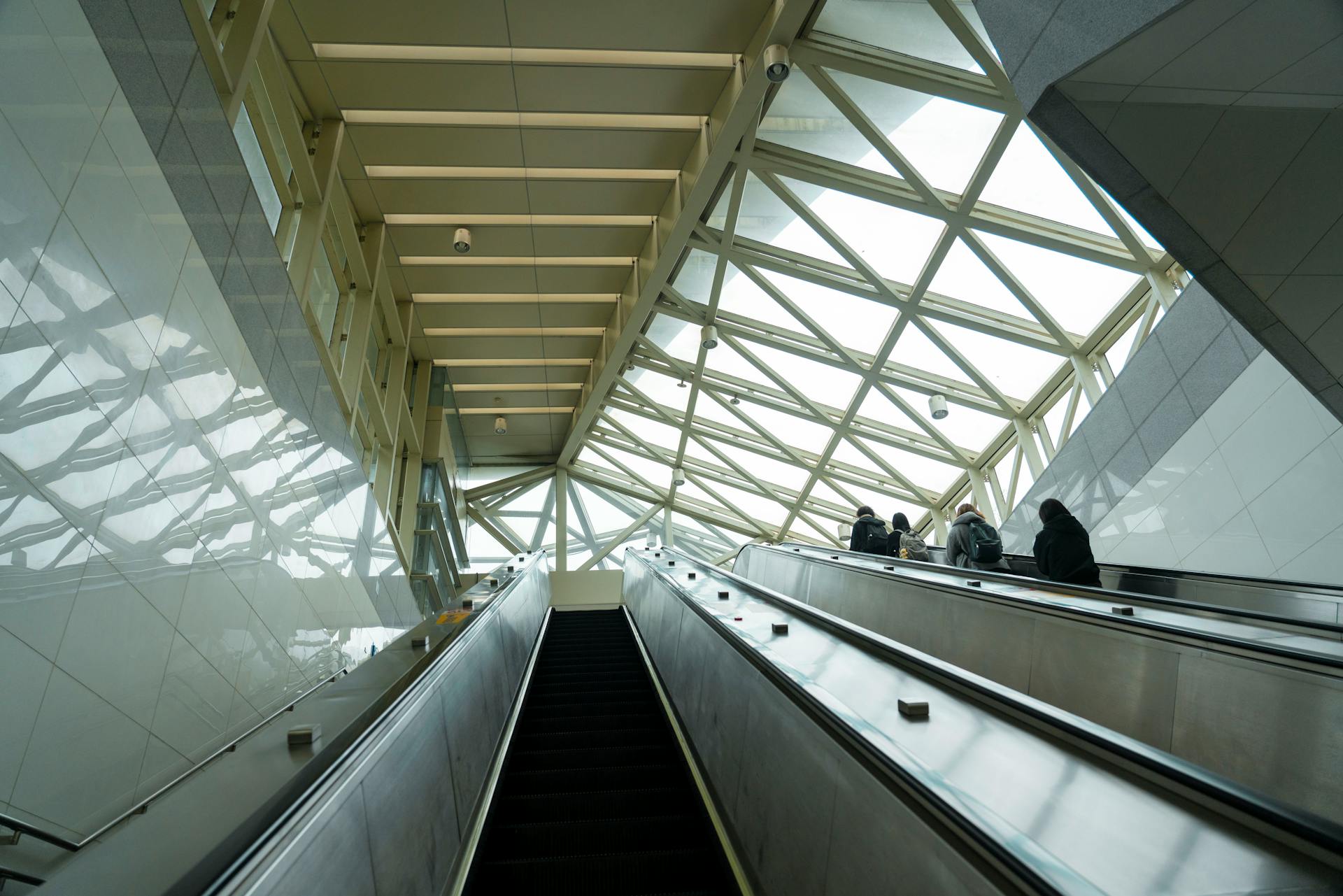 Interior view of a modern terminal featuring escalators and large windows with people traveling.