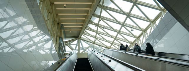 Interior view of a modern terminal featuring escalators and large windows with people traveling.