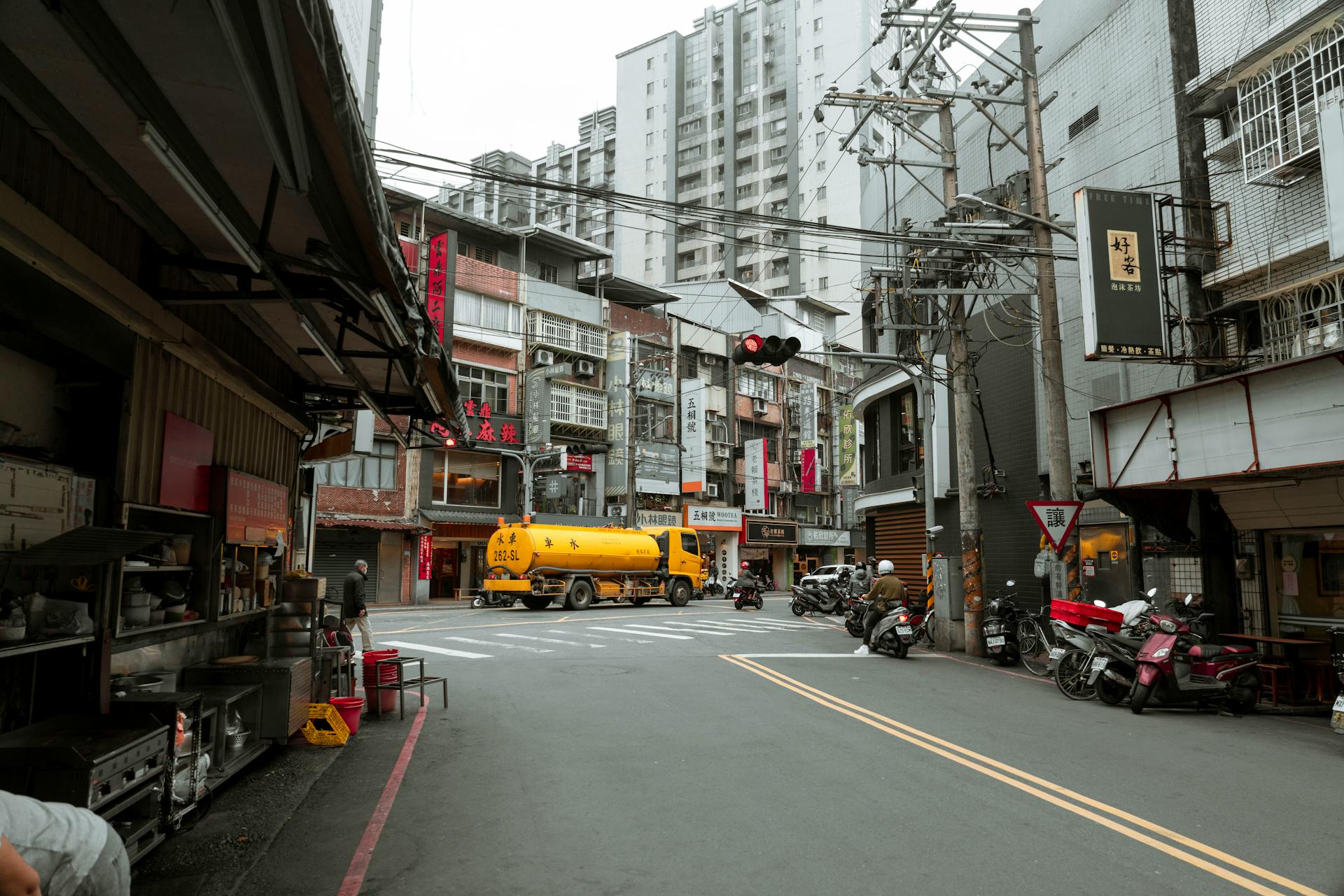 Dynamic urban street view featuring motor scooters and a yellow truck under city skyscrapers.