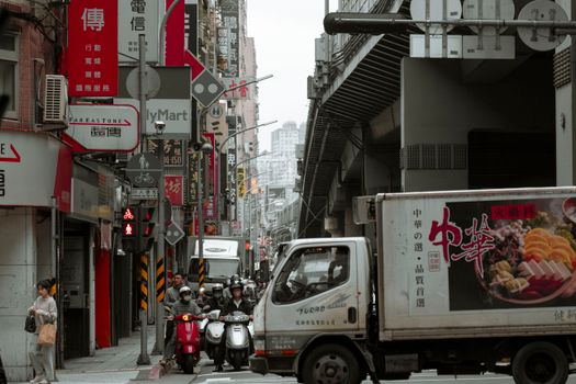 Busy urban scene in an Asian city with motor scooters and a truck on a lively street