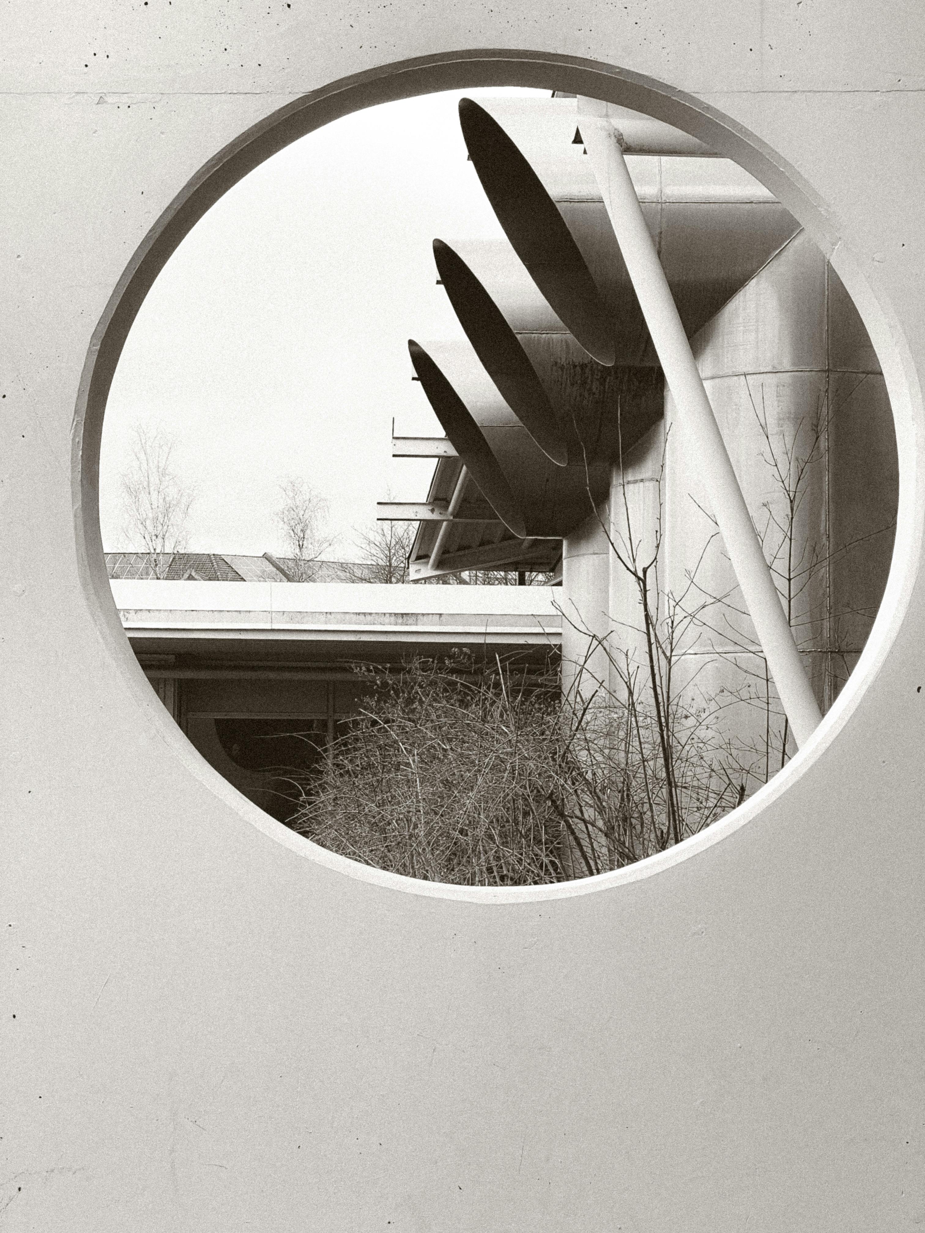 Artistic view of industrial structures through a circular window, showcasing modern design.