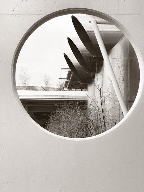 Black and White Photo of Large Pipes Seen through a Circular Hole in a Wall 